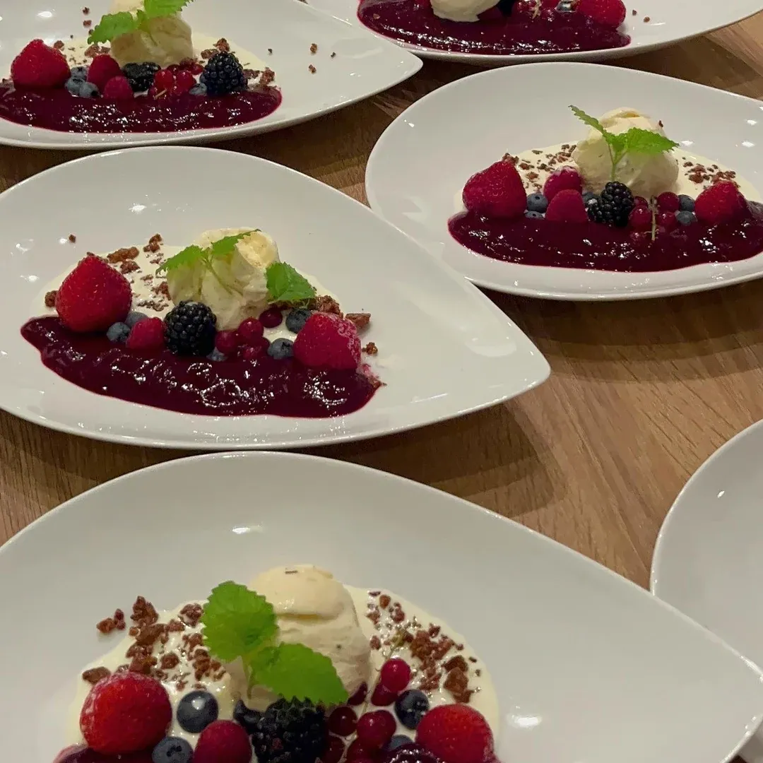 Plates of berry desserts with vanilla ice cream, cream, fresh berries and red berry sauce.