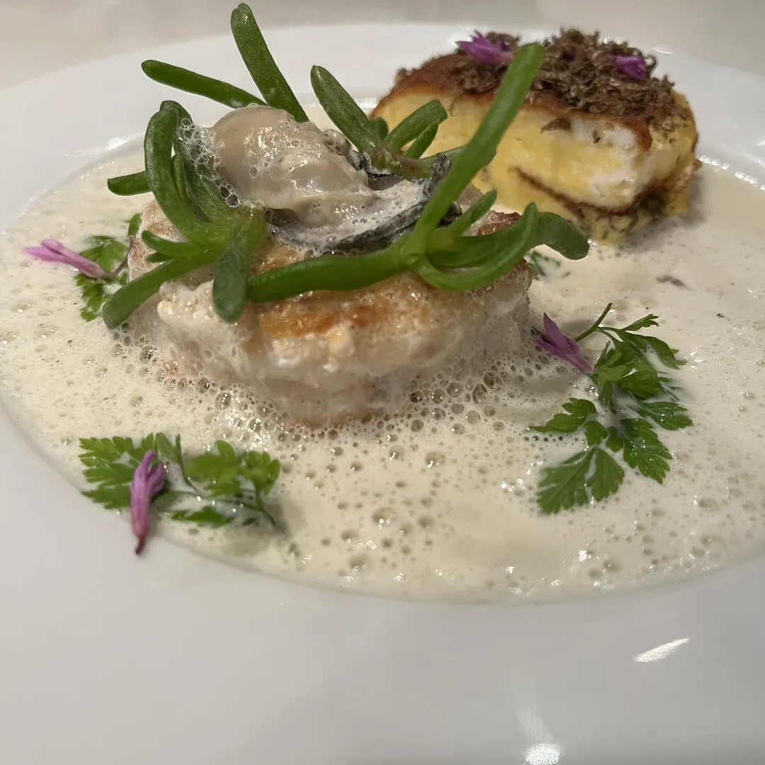 Seared scallops with creamy foam sauce, green beans, herbs, and purple edible flowers on a plate.