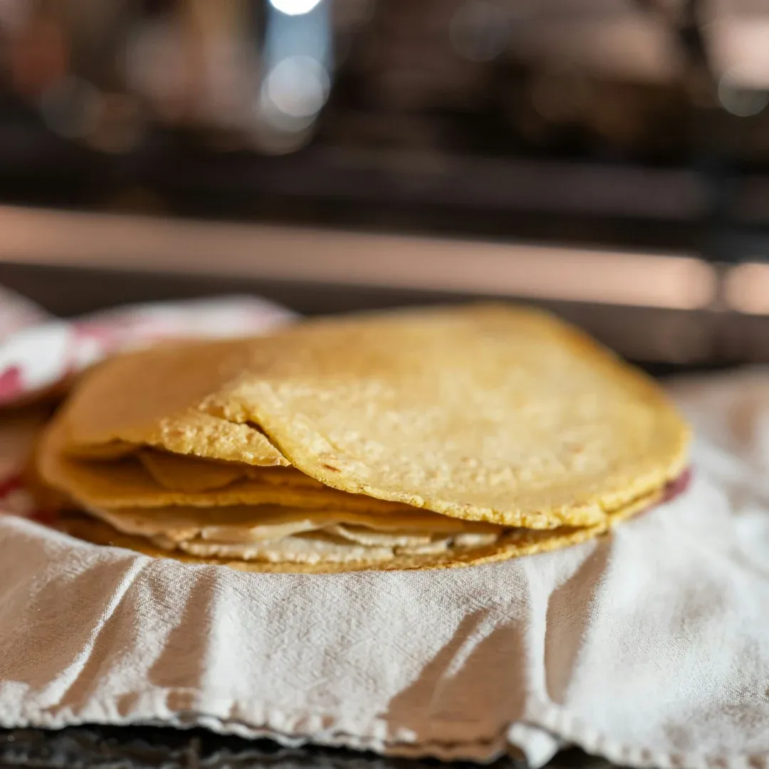 Stack of thin golden corn tortillas resting on a white cloth.
