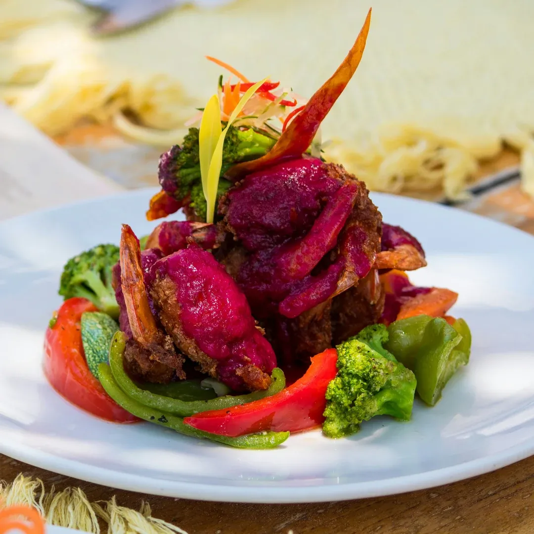 Gourmet plate: crispy fried meat with purple beet glaze, surrounded by broccoli, bell peppers, and snap peas.