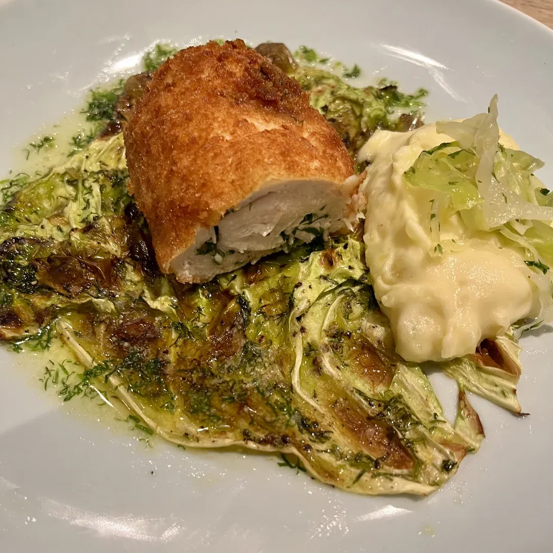 Crispy breaded chicken breast perched on a bed of dill-infused creamed cabbage, with mashed potatoes and shredded cabbage on the side.