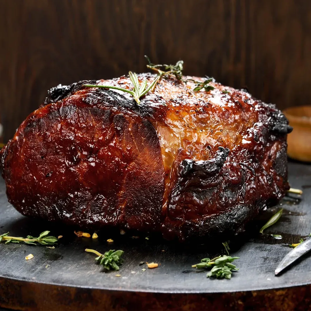 Herb-crusted roasted beef on a dark board with rosemary sprigs on top.