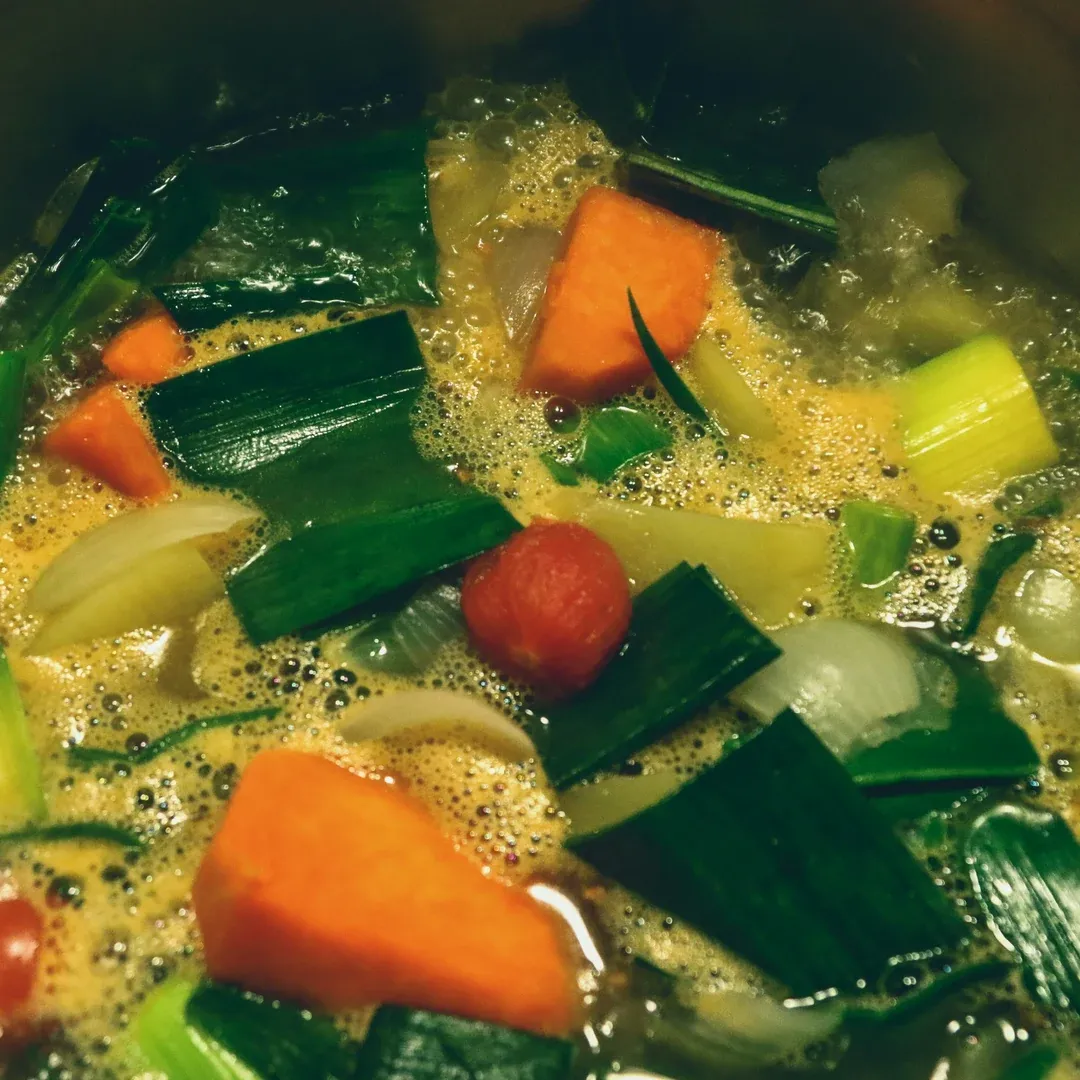 A pot of bubbling vegetable soup with carrot chunks, leeks, onions, and greens simmering in broth.